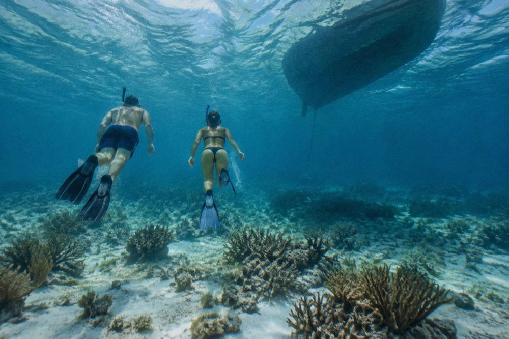 Snorkelers in the water beside a moored boat above a shallow reef