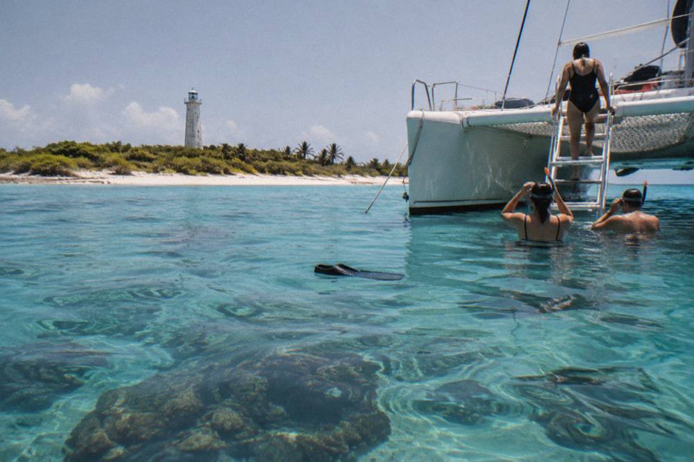 A catamaran anchored near a reef with passengers preparing to enter the water