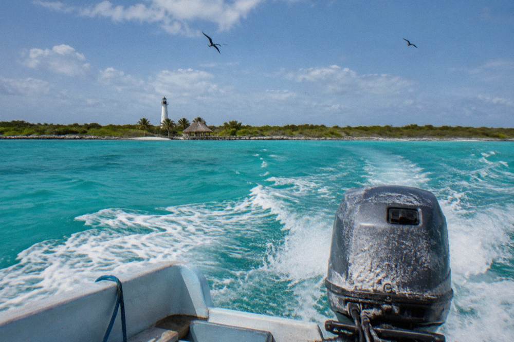 A speedboat crossing open turquoise water toward an island shoreline