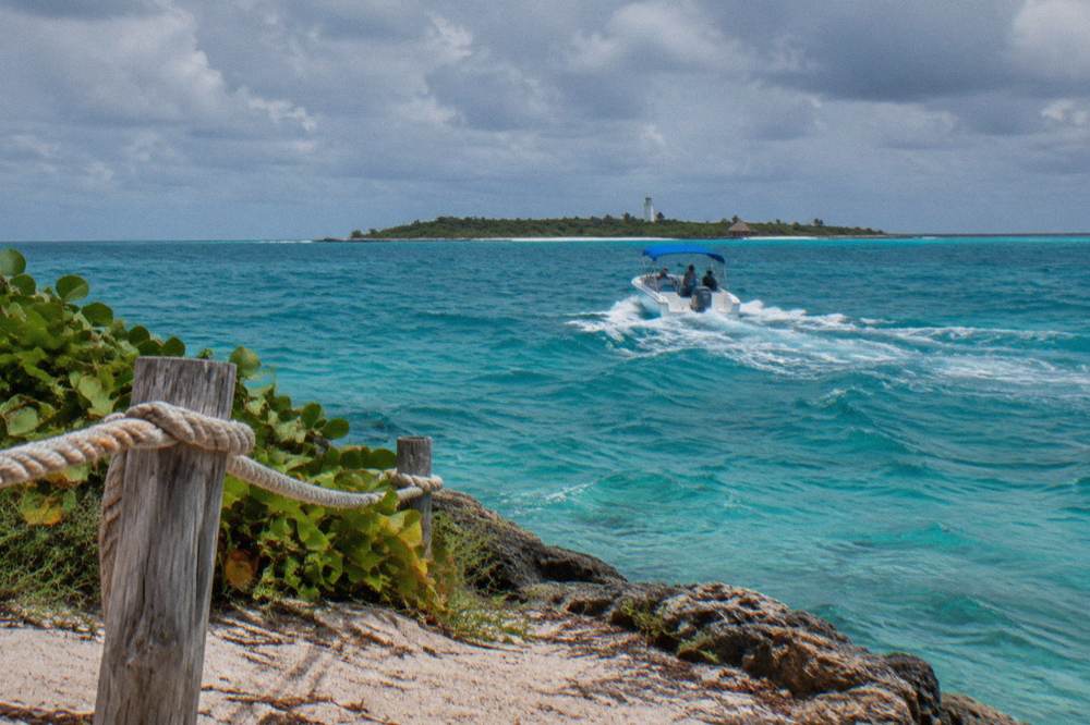 Speedboat crossing open turquoise water toward a low green island on the horizon