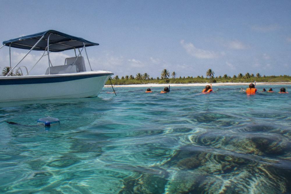 Speedboat anchored beside a shallow reef with snorkelers in life vests in clear water