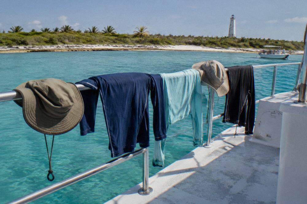 Long sleeve swim shirts and wide brim hats drying on a boat railing in bright sunlight