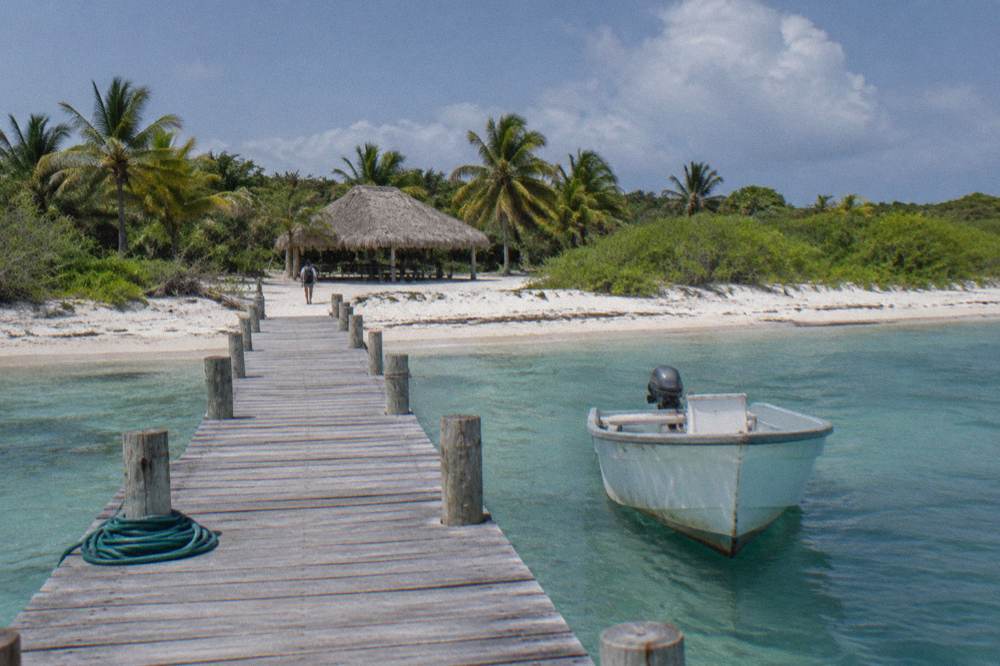 Small boat moored at a wooden island dock with palm thatched palapa behind