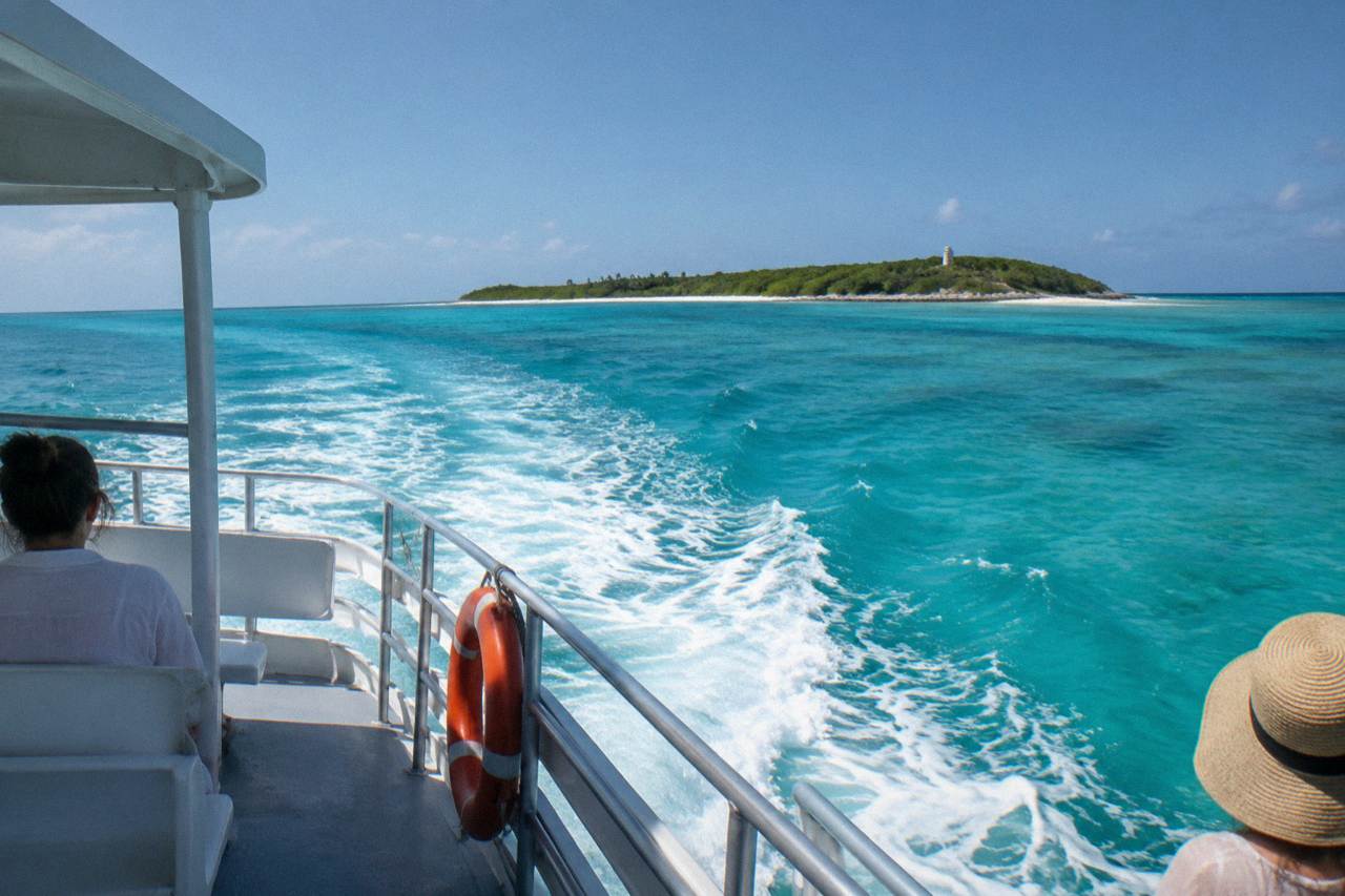 A small boat crossing open turquoise water toward a low green island on the horizon