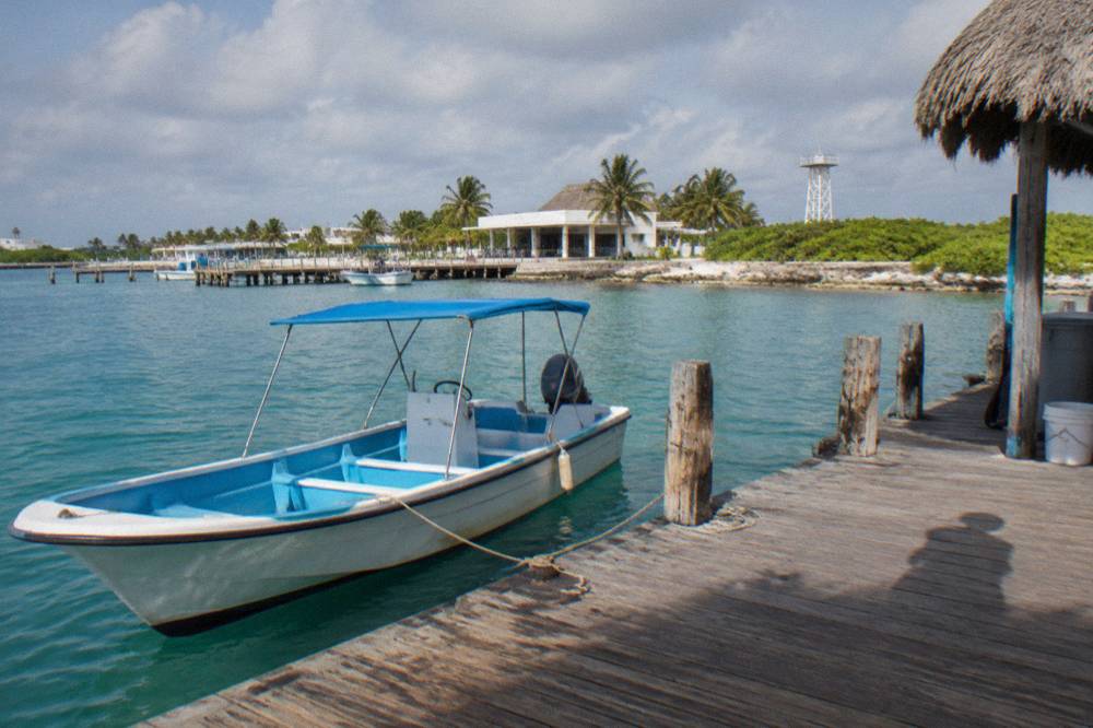 A small speedboat anchored beside a wooden dock on a quiet island shoreline with dune vegetation