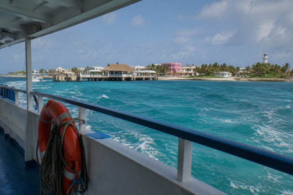 A ferry deck view of turquoise open water with an island town appearing on the horizon