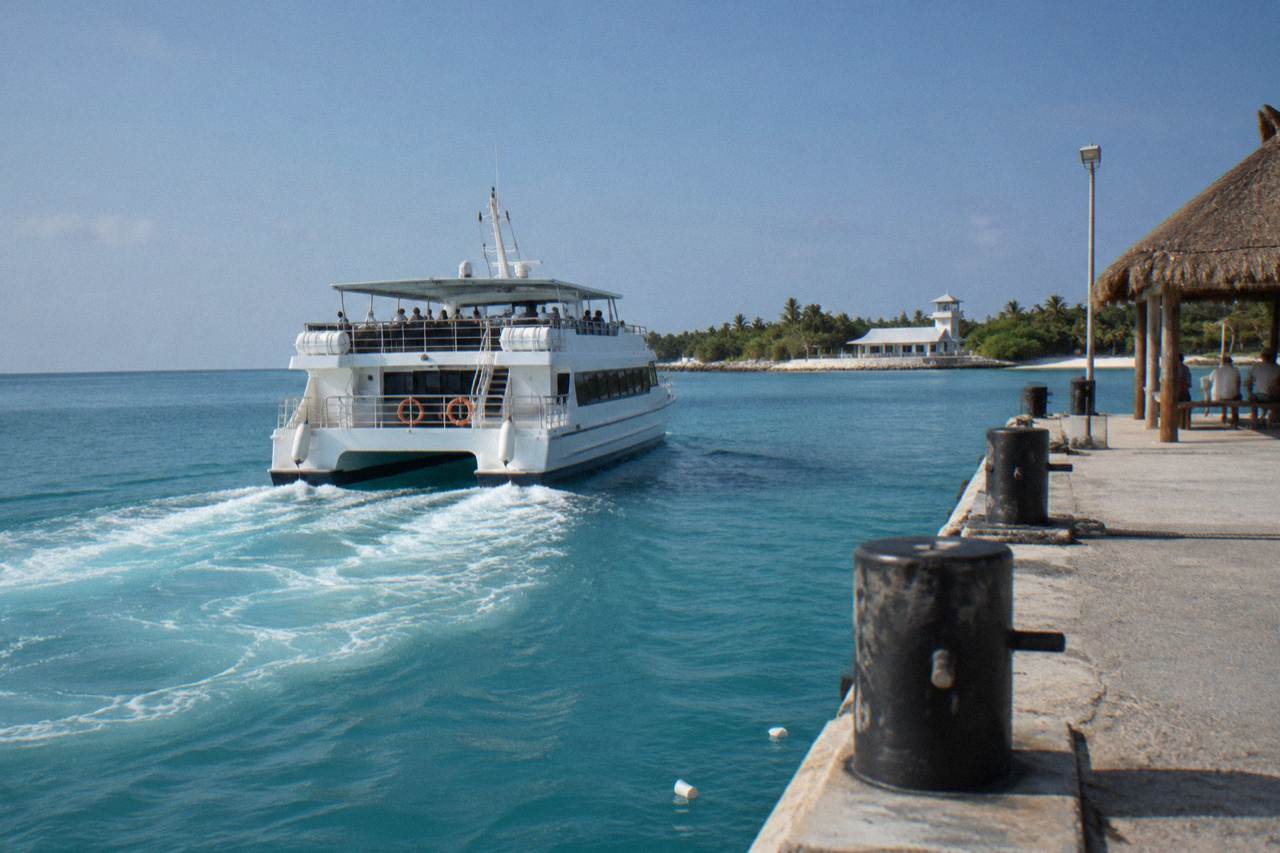 A passenger ferry crossing open turquoise water toward an island coastline under a clear sky