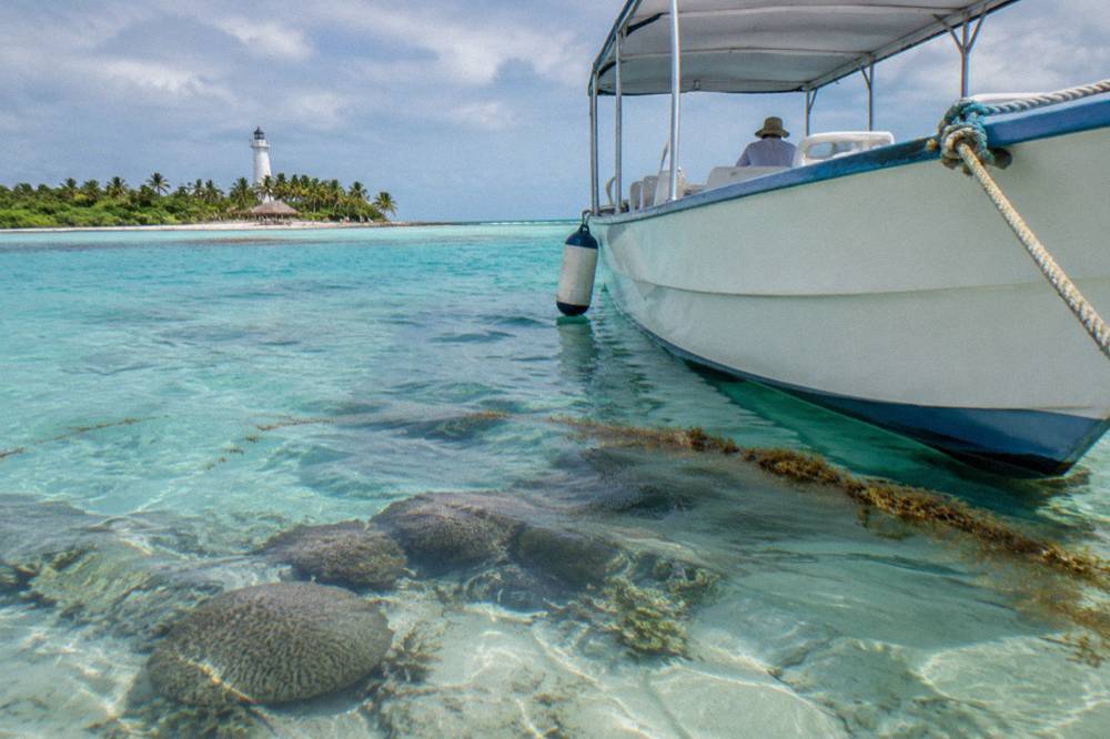 Small white passenger boat moored beside clear shallow water near a reef