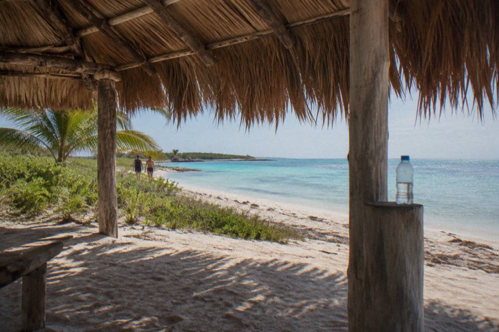 Palm thatched palapa shade structure on a white sand beach beside shallow clear water