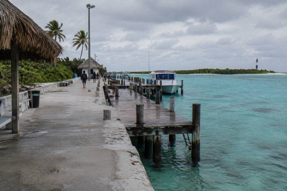 A wooden pier extending over clear shallow water under scattered clouds