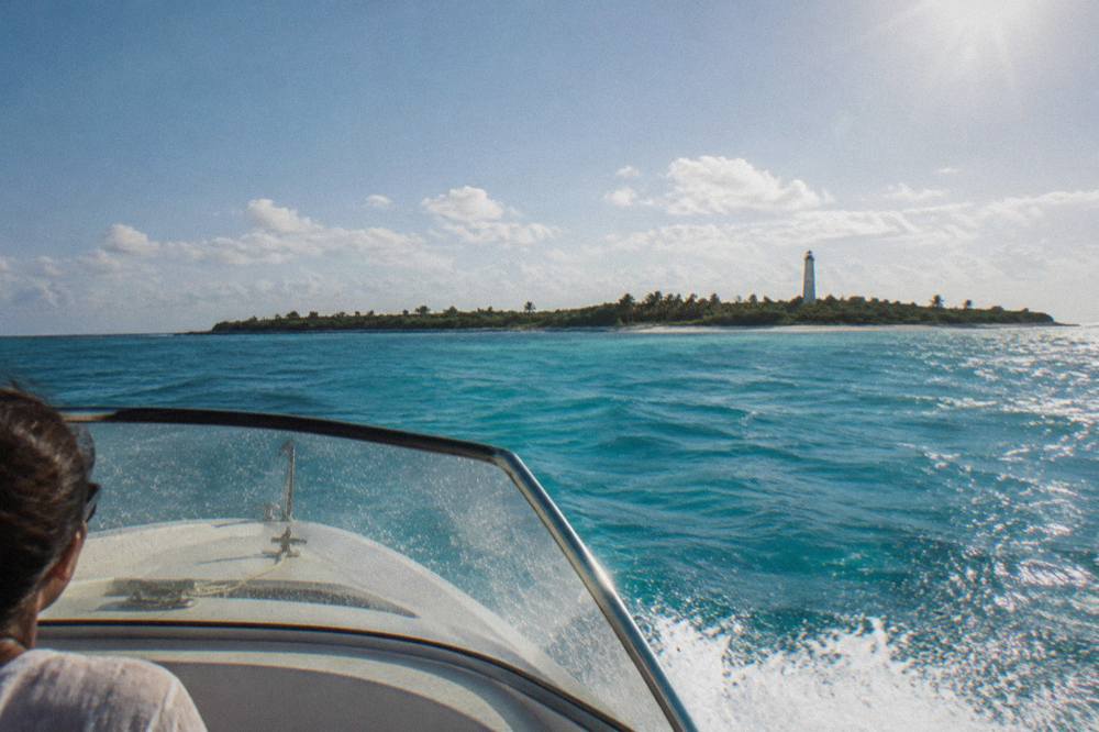 A speedboat crossing open turquoise water toward a low green island on the horizon