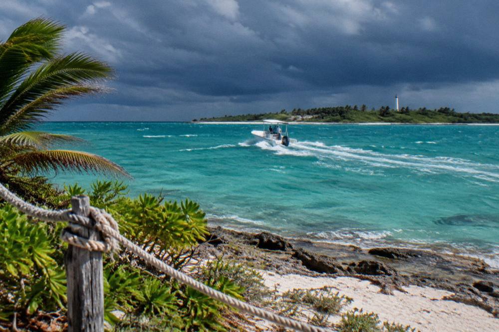 White speedboat crossing open turquoise sea toward a low green island on the horizon