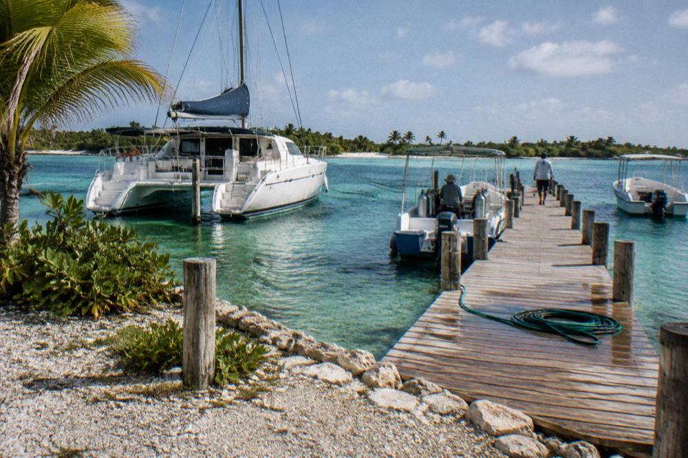 Catamaran and small boats moored in clear shallow water beside a wooden dock at a marina