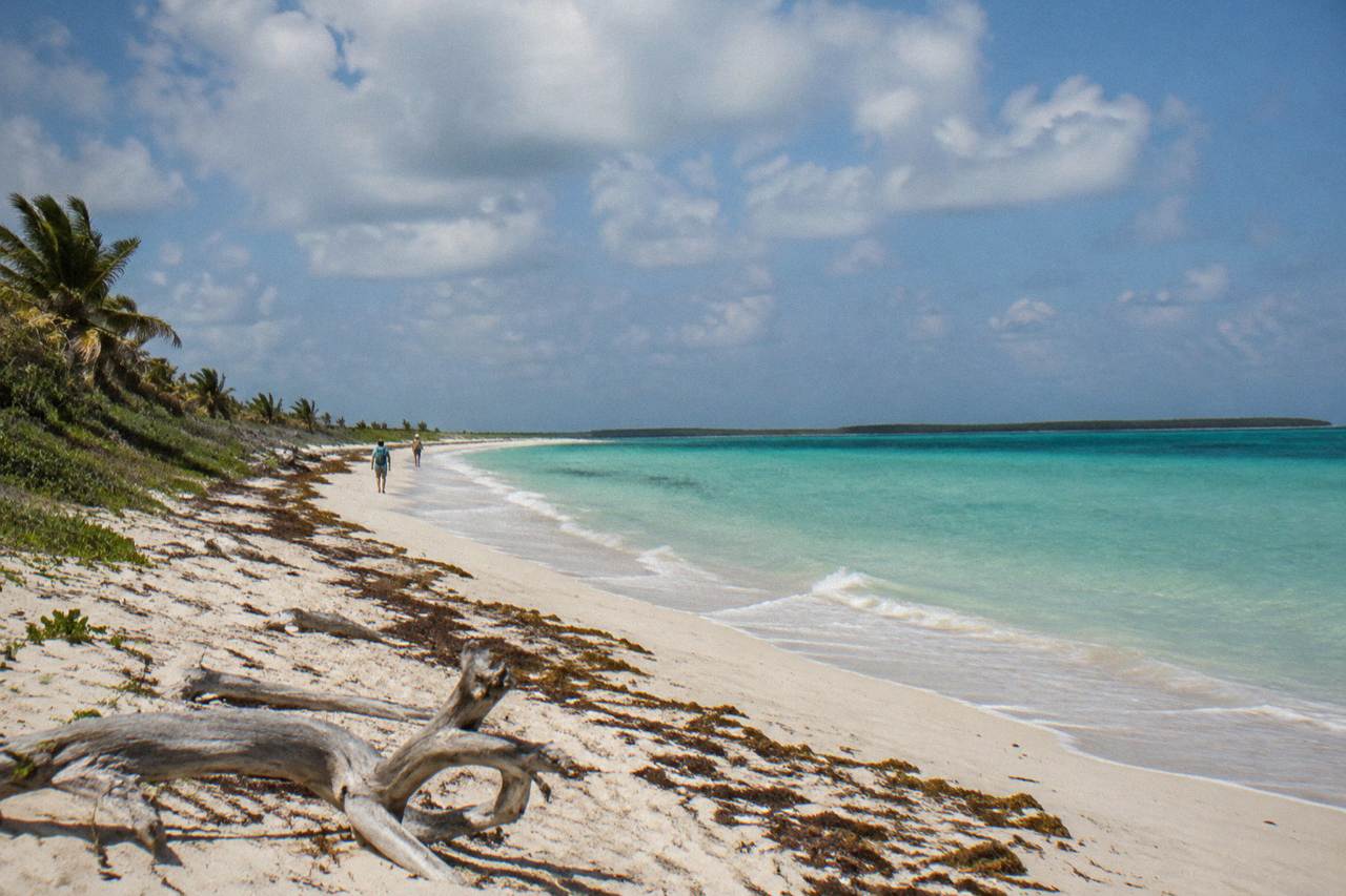Empty white sand beach and calm turquoise water at a small tropical island under scattered clouds