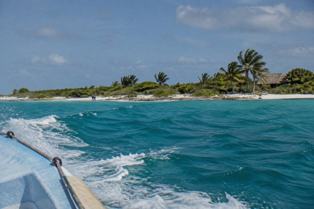A speedboat cutting across open turquoise water toward a distant low island