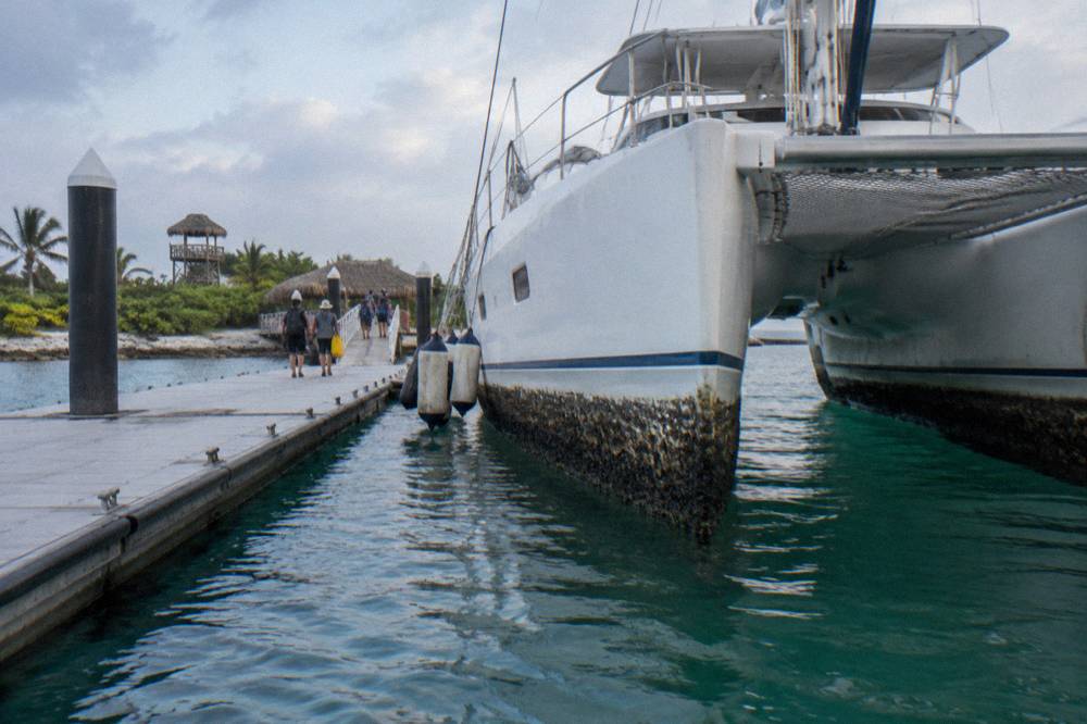 A double-deck catamaran moored at a marina pier with passengers boarding