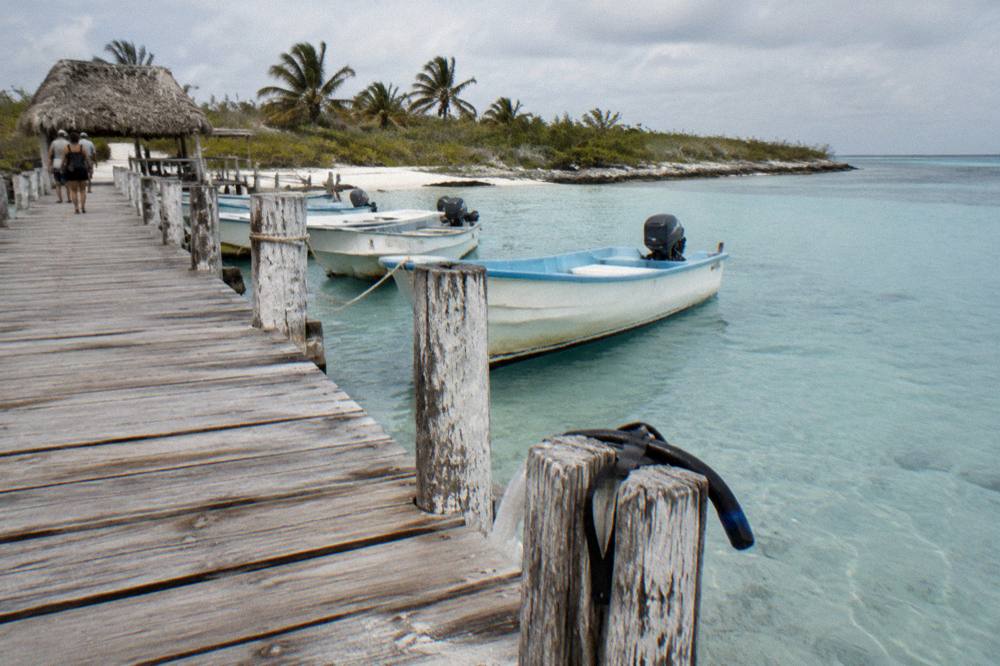 A wooden pier with small boats tied up and clear shallow water below