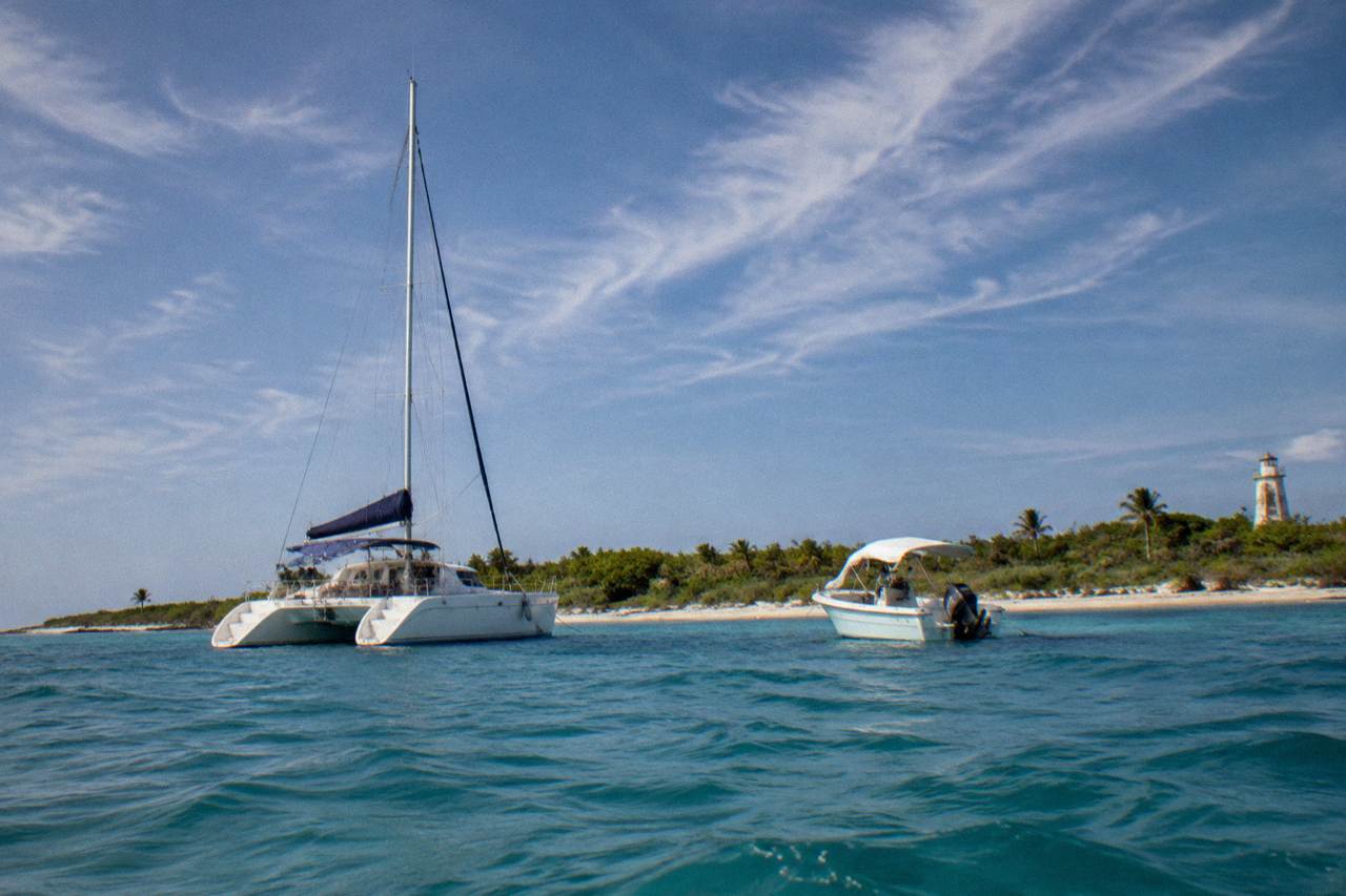 A sailing catamaran and a small speedboat anchored near a low green island under a wide sky