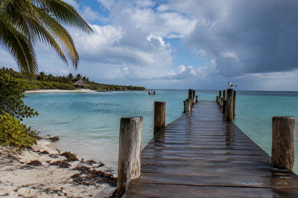 Wooden dock extending into calm turquoise Caribbean water under a partly cloudy sky