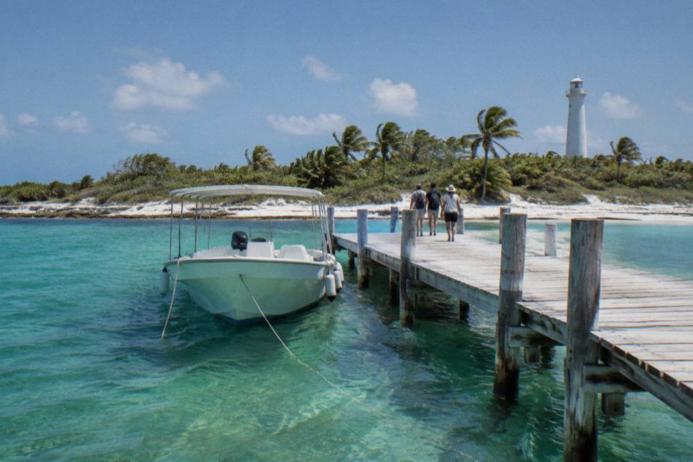 A small white passenger boat moored at a wooden dock over clear shallow water