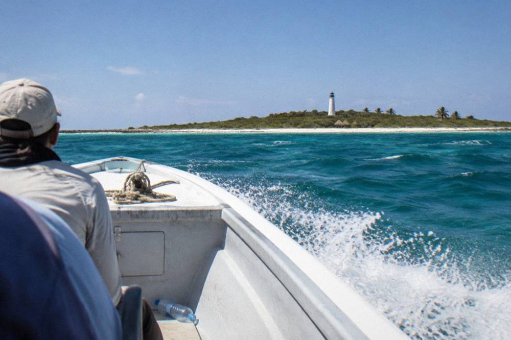 A speedboat crossing open turquoise water toward a low green island on the horizon