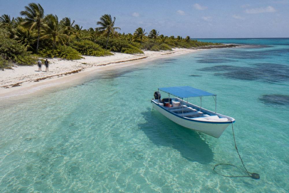 A small boat anchored off a palm-lined island beach in clear shallow water