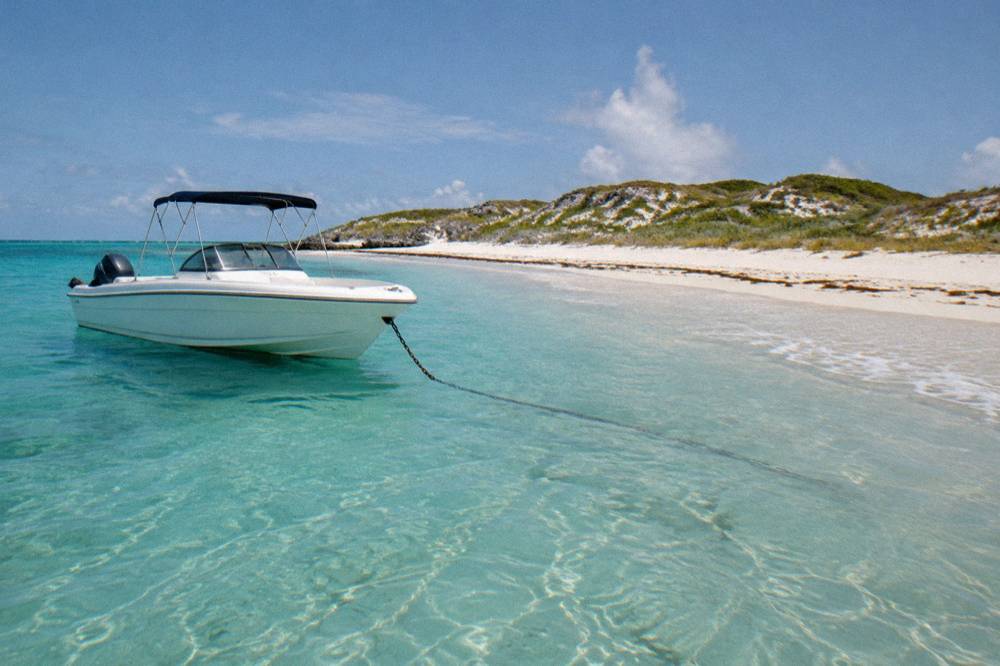 White speedboat anchored off a empty Caribbean beach with palm-free dunes