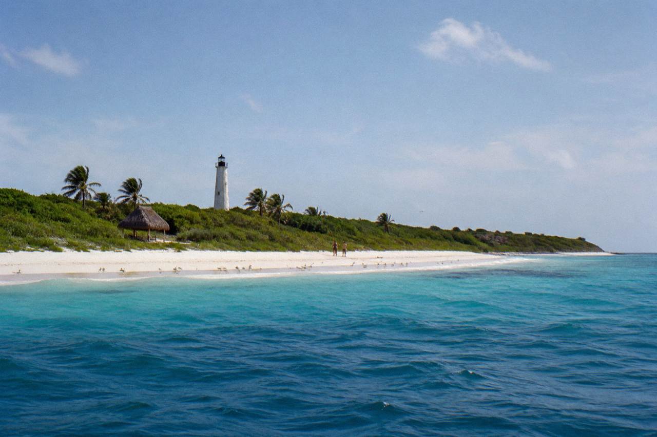 Low sandy island with white beach, turquoise water and dense green scrub under a wide sky