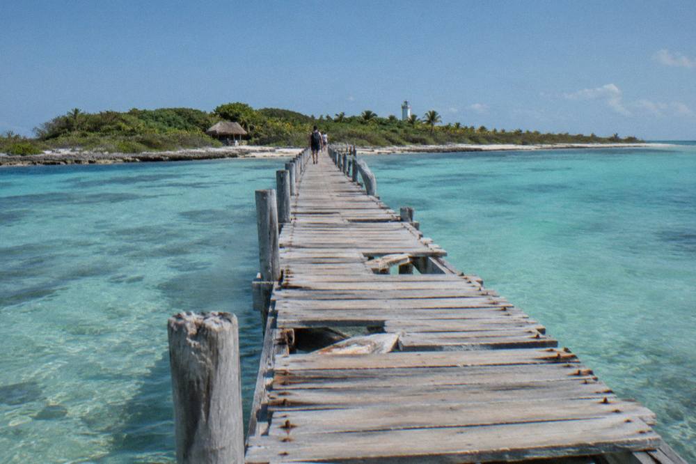 A wooden pier stretching toward a small green island across calm turquoise water