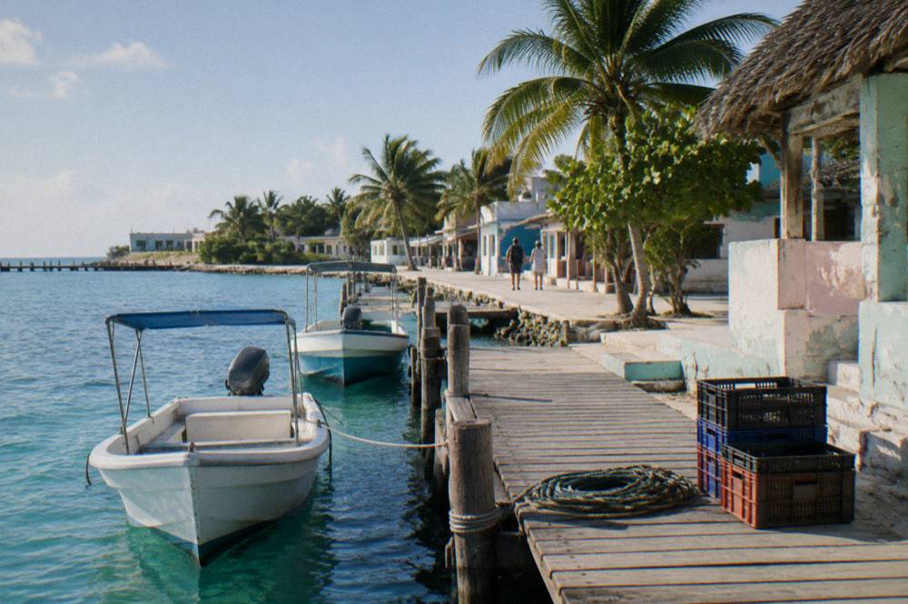 A small dock with moored boats and a storefront on a sunny island street