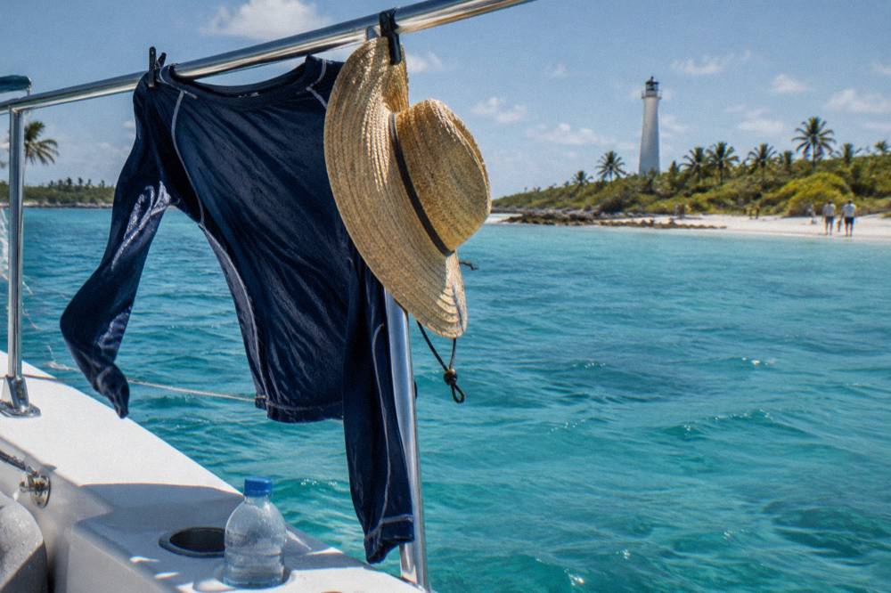 A long sleeve rash guard and hat drying on a boat rail in bright sunlight