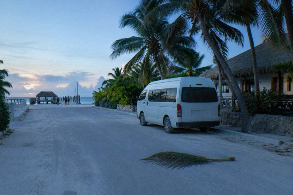 Hotel zone street in early morning light with a van waiting beside palm trees