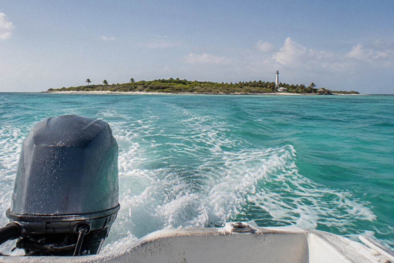 Speedboat on open turquoise water heading toward a low green island on the horizon