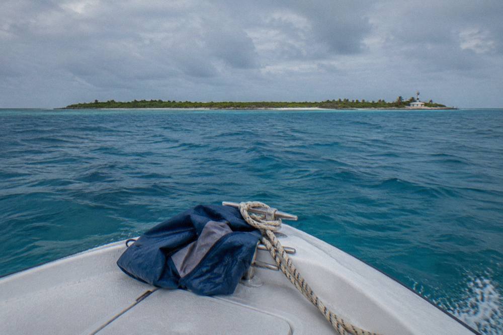 Open blue water horizon seen from the bow of a small boat heading north toward a low green island
