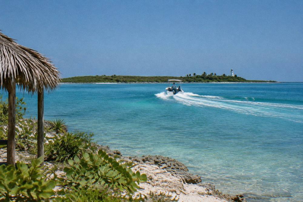 Speedboat cutting across open turquoise water toward a low green island on the horizon
