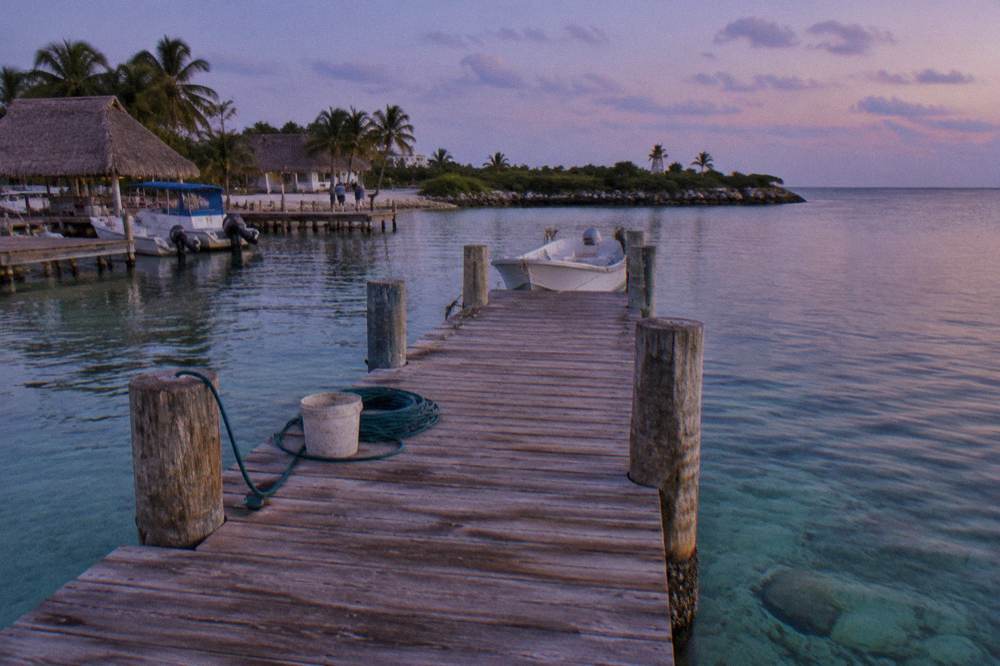 Wooden pier extending into clear shallow water with a small white boat moored at the end