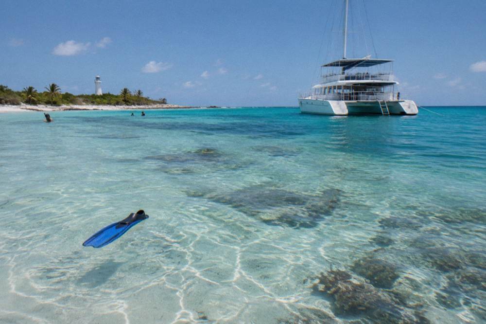 Anchored catamaran seen from a sandy beach with shallow clear water