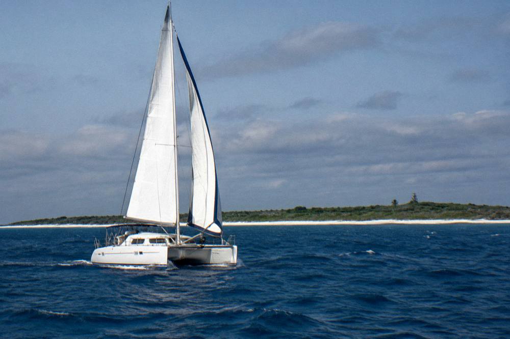 A catamaran under sail on open blue water with low clouds on the horizon