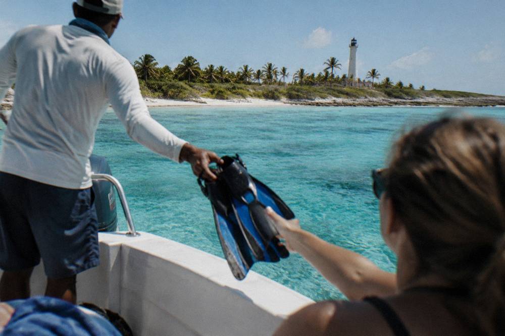 A crew member handing snorkel fins to a passenger at the stern of a boat