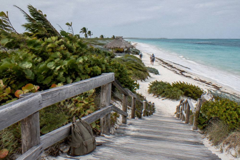 A small canvas backpack and empty hands on a weathered wooden walkway over sand dunes